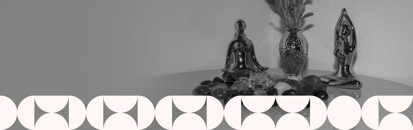 Estátuas em posição de meditação sobre pedras, ao lado de um vaso com flores