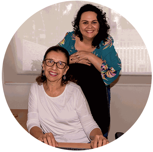 Duas profissionais da clínica sorrindo, uma sentada e outra em pé atrás
